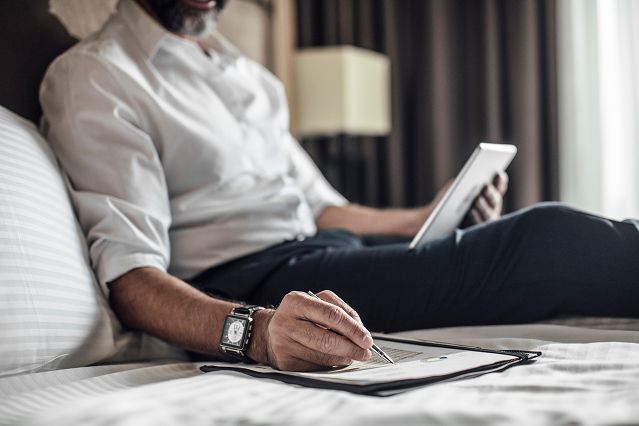 Ein Mann sitzt bequem auf einem Bett und benutzt ein Tablet und einen Stift zum Schreiben